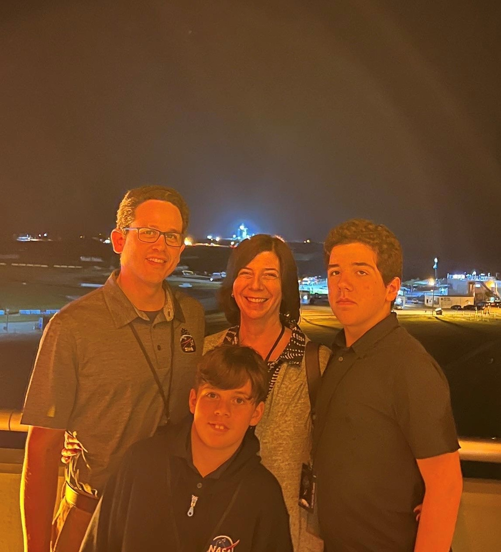 Four people gathered for a group photo at night with a well-lit building behind them. 